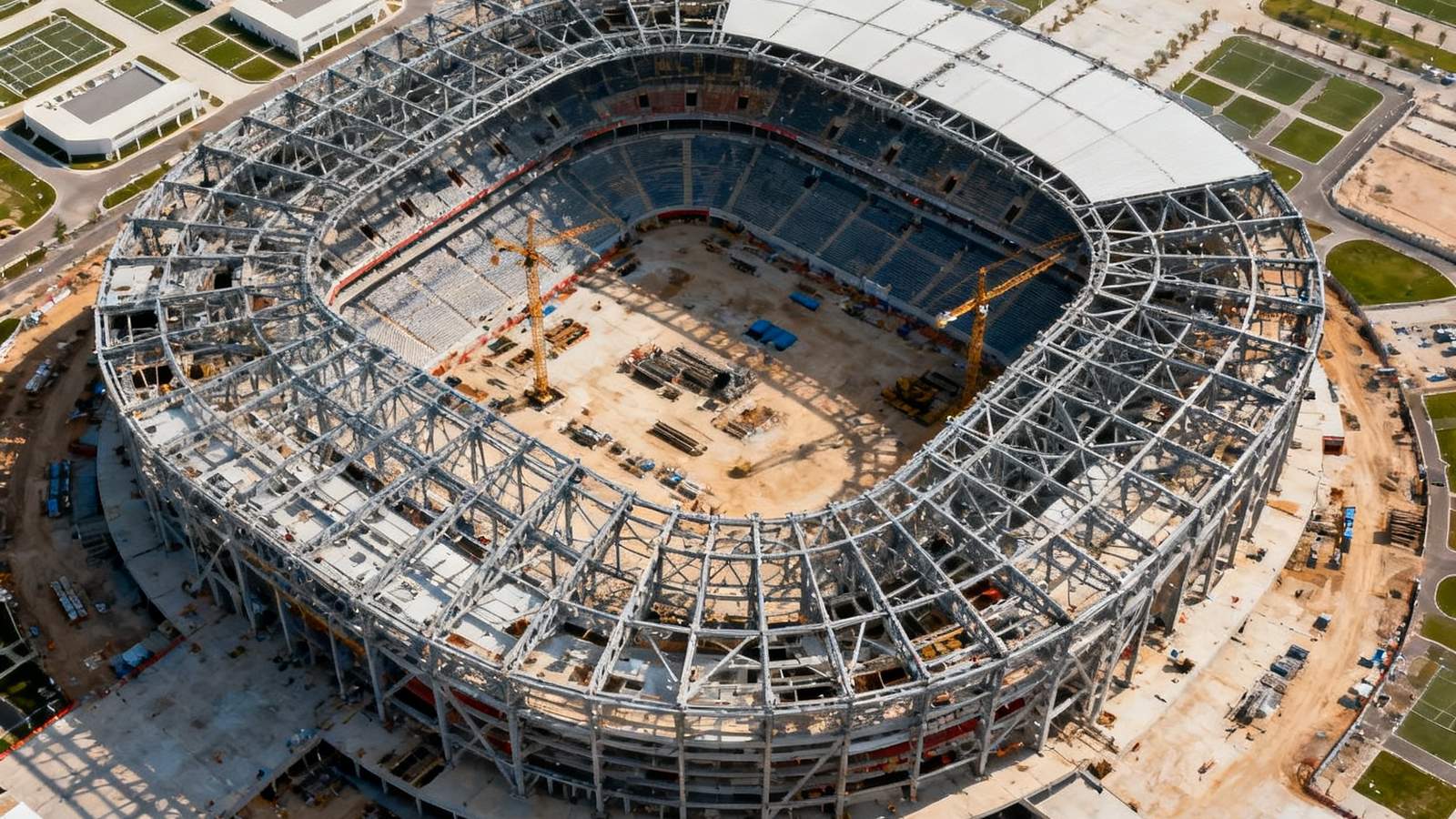 无人机航拍视角下的2026年世界杯新建场馆施工现场，钢结构骨架已基本完成，周围是规划整齐的配套设施区域